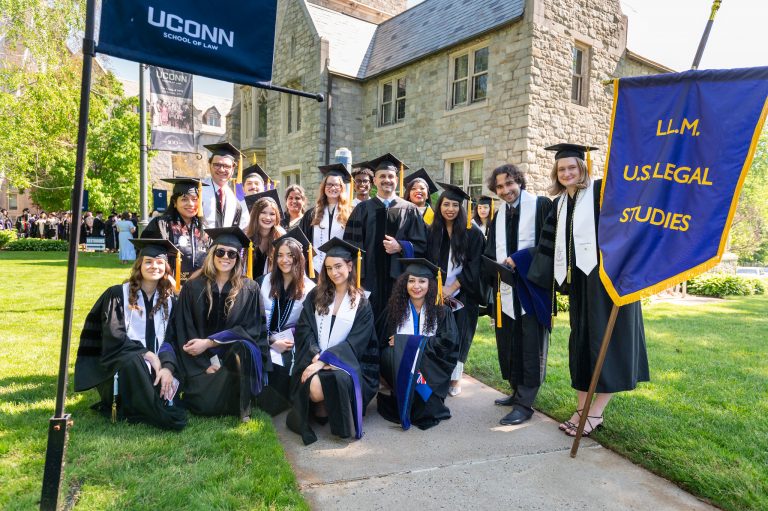 A group of graduates stand on the lawn. One is holding a banner that says LLM US Legal Studies