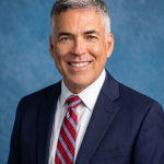 Man in blue suit smiling in front of blue background