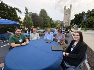Five students sit at a round table outside with Starr Hall in the background.