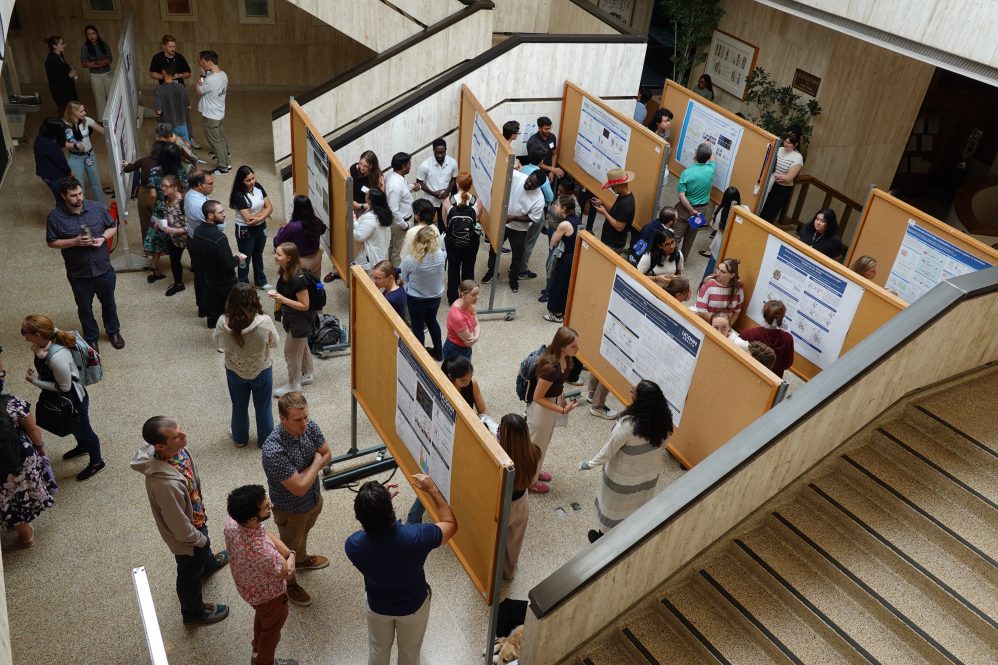Overhead view taken from a balcony of people viewing research posters on the exhibit floor below.