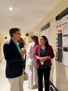 Two people discuss a research poster hanging on the wall in a hallway.