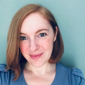 A woman wearing a blue shirt appears for a portrait in front of a blue background.