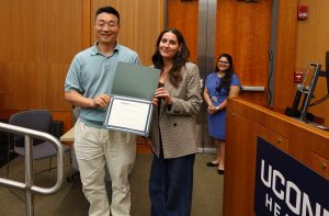 A man on the left and a woman on the right hold an award certificate between them.