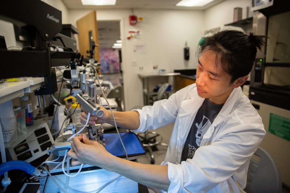 A researcher in a lab coat works with a microscope