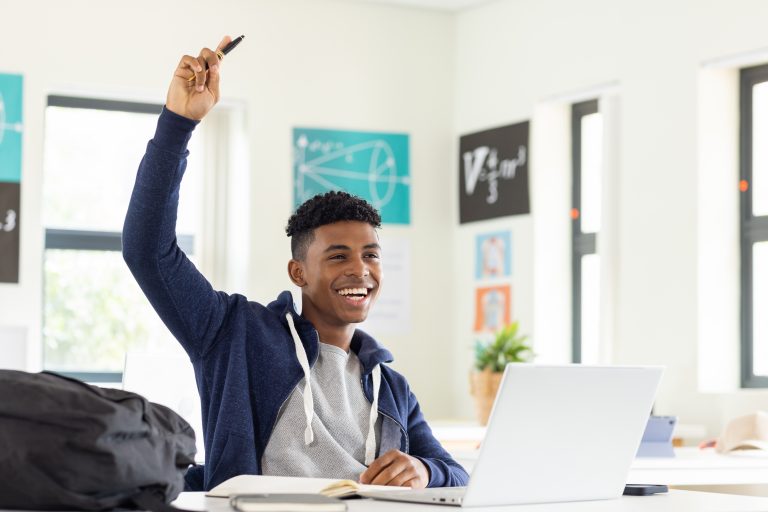 High school student with laptop raising his hand in class