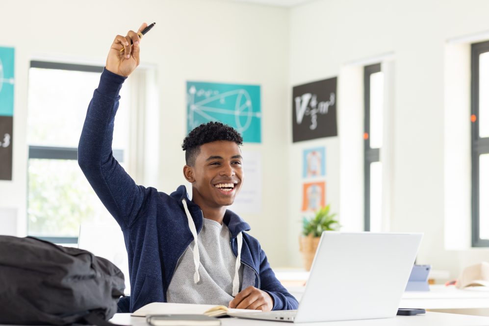High school student with laptop raising his hand in class