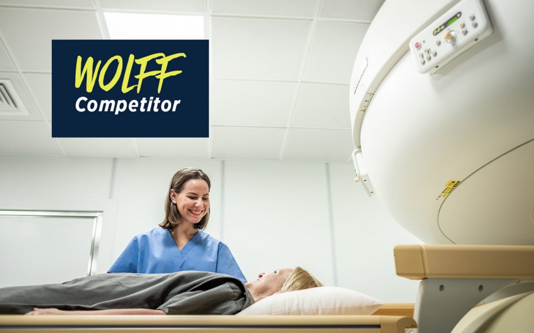 A technician in medical scrubs smiles down at a patient about to be moved into a radiation machine.