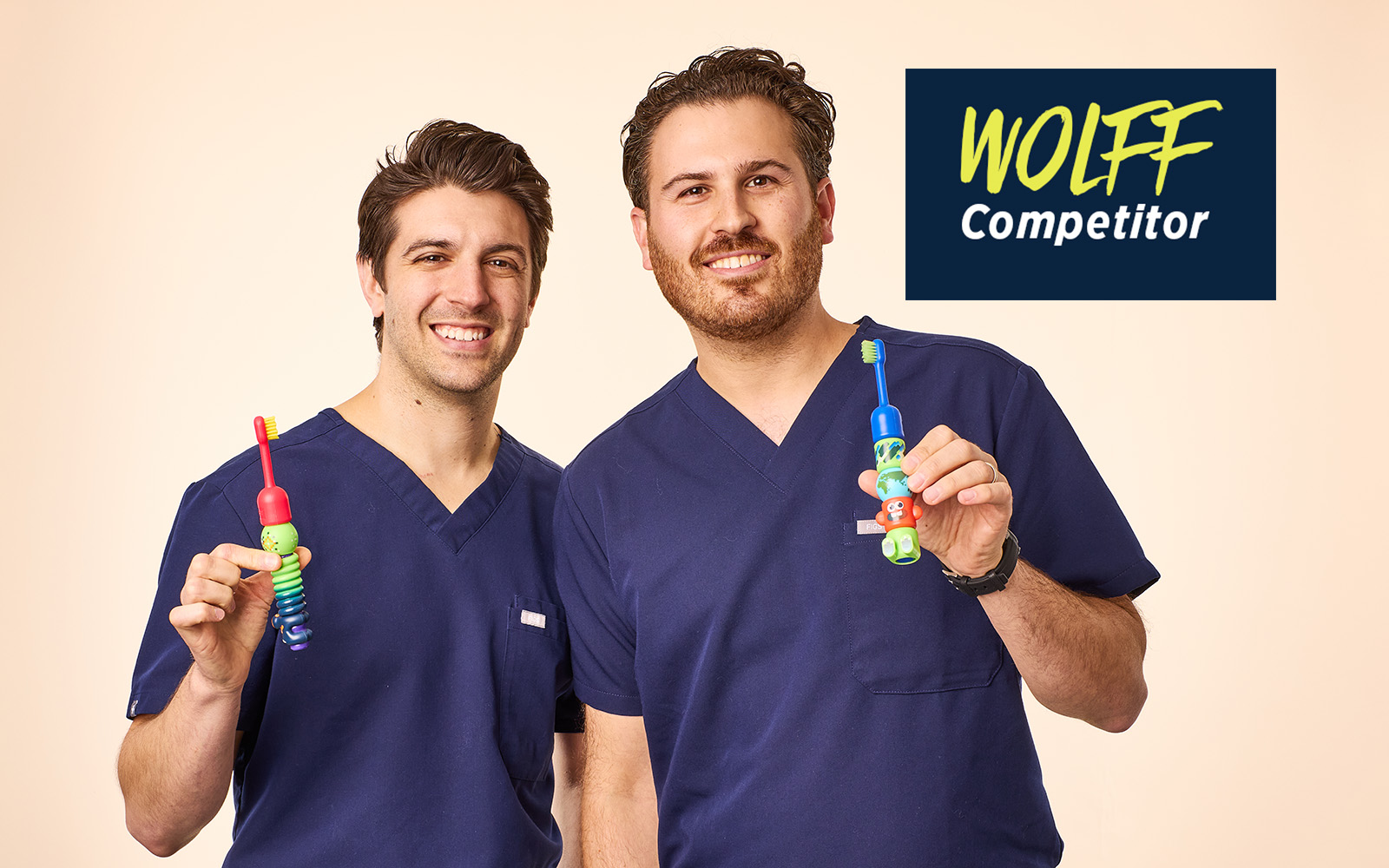Dr. Dante Paolino and Dr. Zachary Gelber, in blue medical scrubs, each holding a Build-a-Brush toothbrush.
