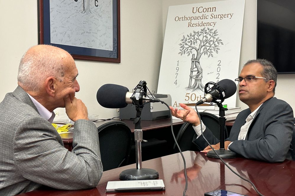 two men speaking to each other behind tabletop microphones