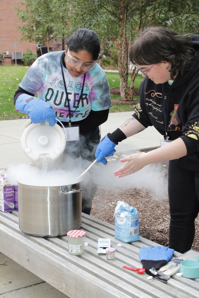 Two people wearing gloves and scooping from a bucket of liquid nitrogen producing steam