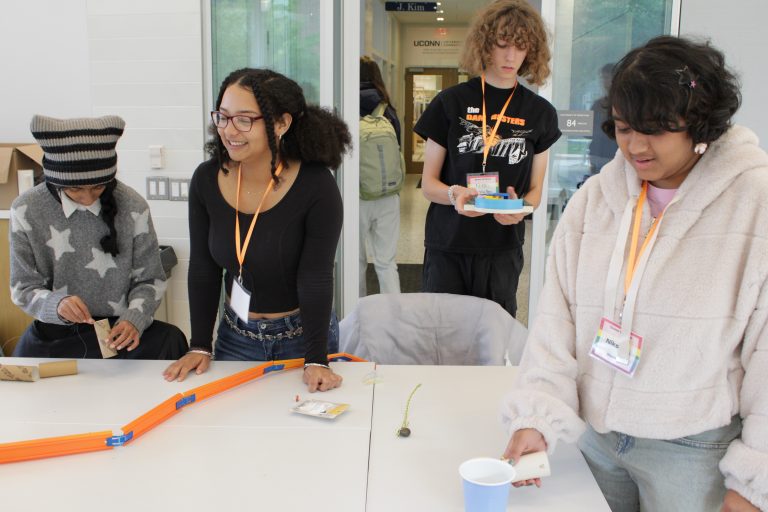 High schoolers smiling as they work with pieces of a Rube Goldberg machine