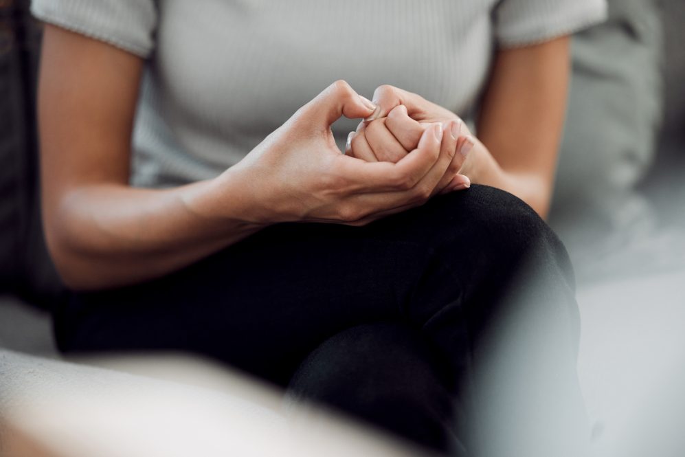 woman sitting alone and feeling anxious while picking the skin on her nails