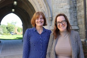 Two women stand in front of an archway on the UConn Law campus.