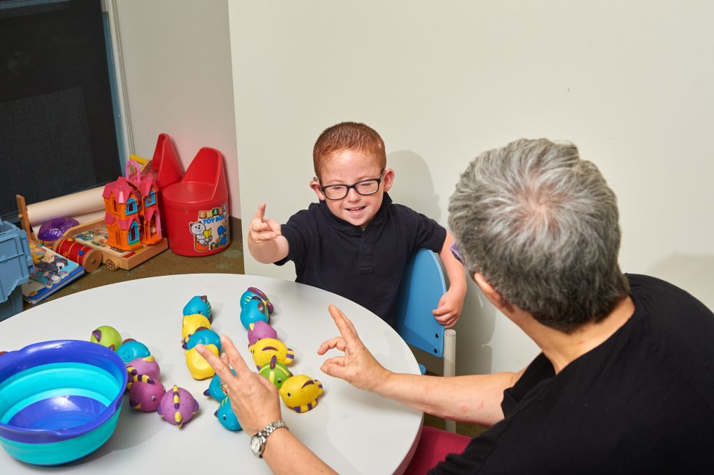 A woman signing to a deaf child while toys lay on a table