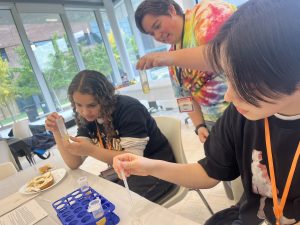 A volunteer in a tie-dye shirt holding up a test tube with students who are working with pipettes