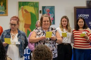 four women and a man reciting a pledge, reading off a yellow card