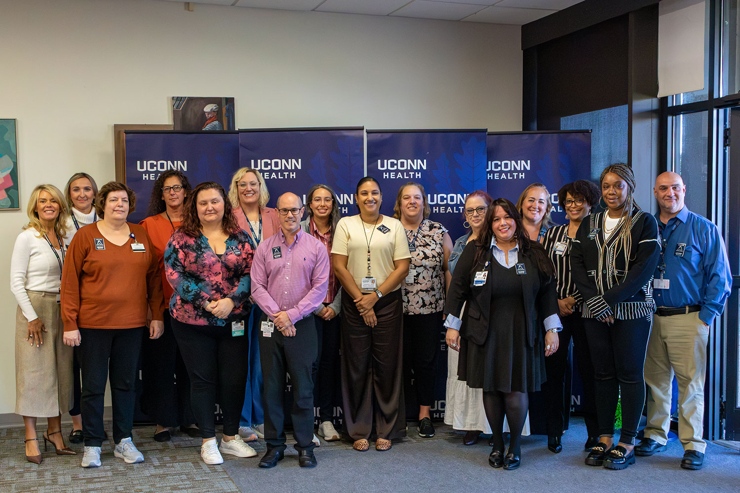 group portrait of 16 indoors in front of UConn Health banners
