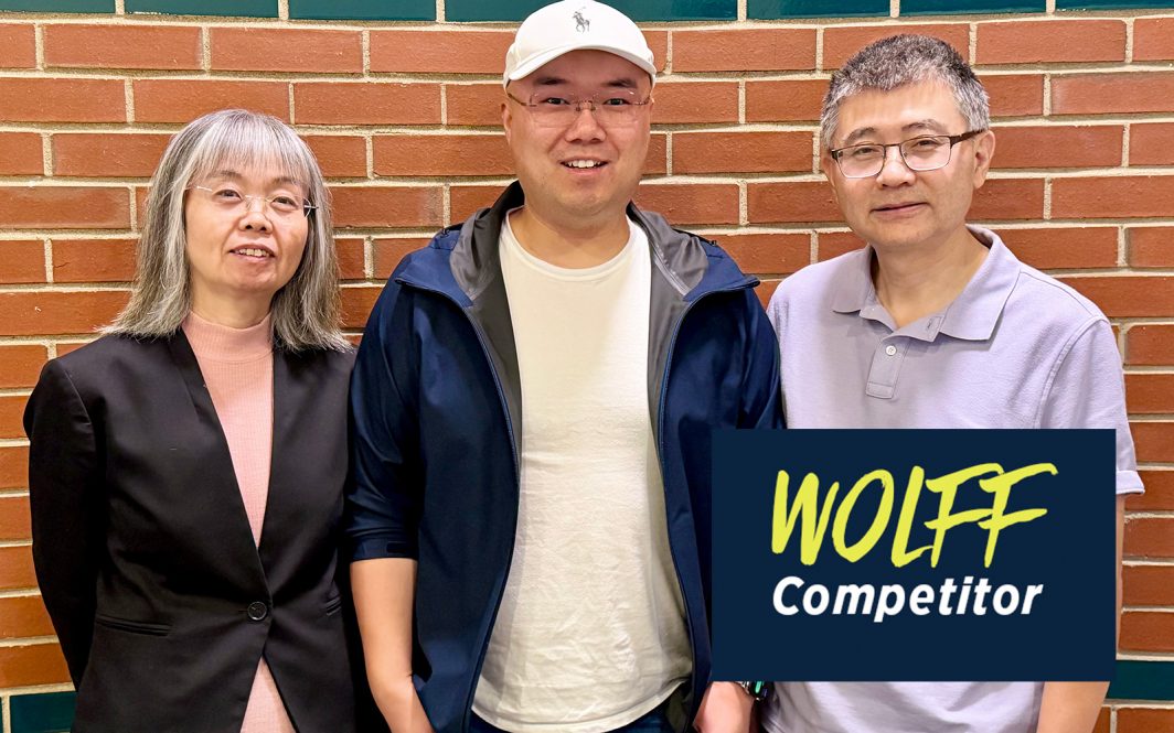 Three people pose for a group photo in front of a brick wall.