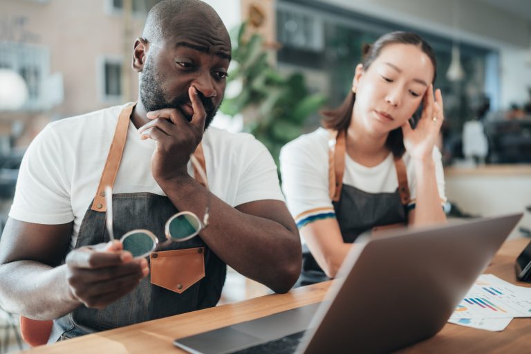 Two baristas with worried expressions look at a laptop.