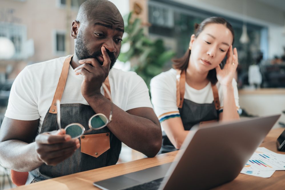 Two baristas with worried expressions look at a laptop.